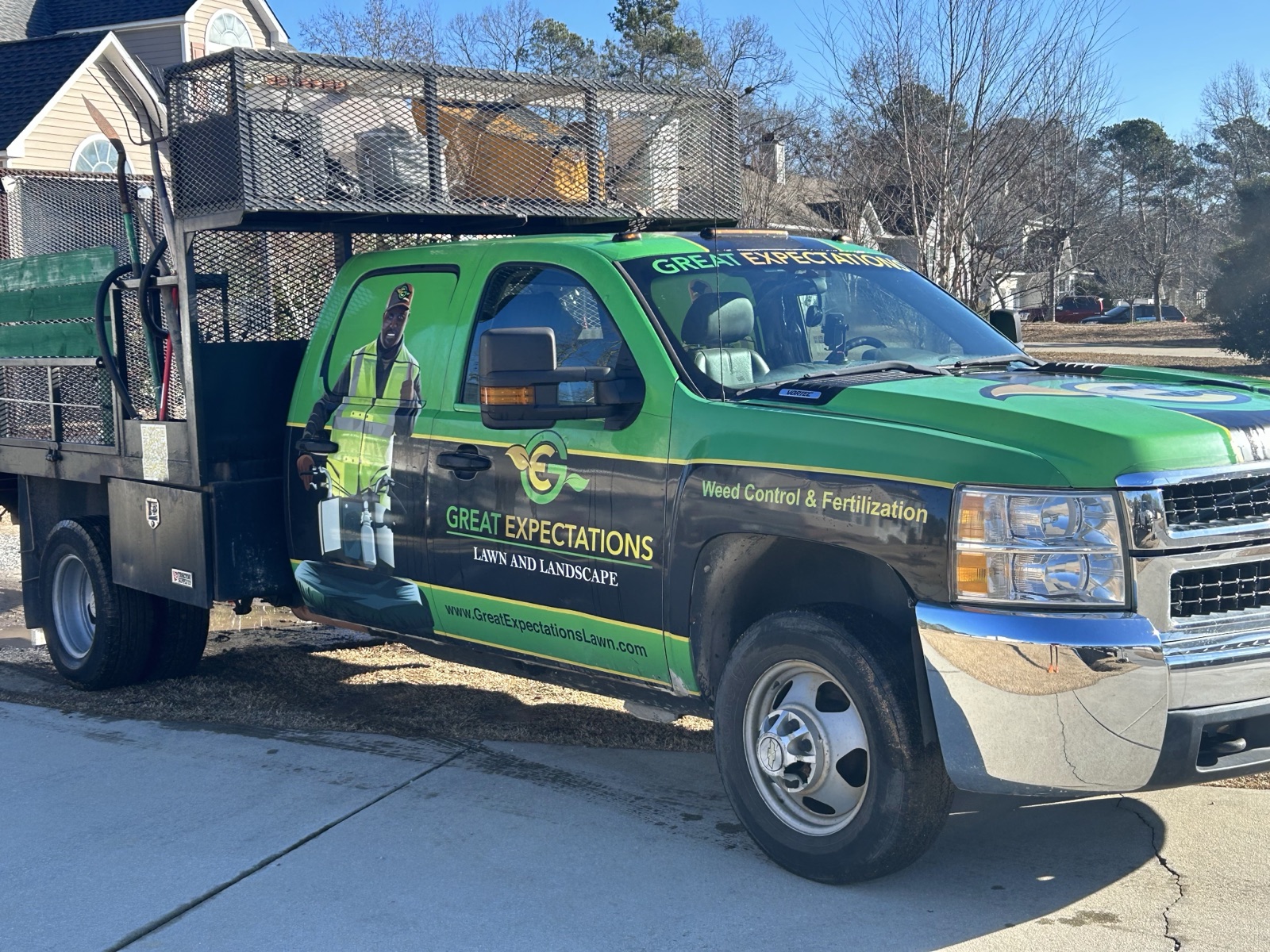The company's green-wrapped work truck — 'Weed Control & Fertilization' — the same crew and the same standard pulling up to every lawn on the schedule.