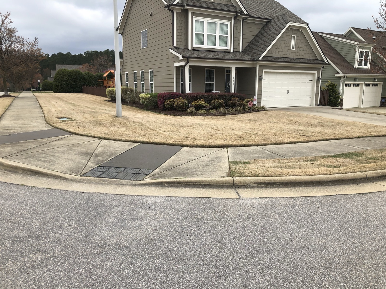A dormant, thinning corner lot at the start of a program — the honest 'before' that a season of feeding, weed control and overseeding is built to turn around.